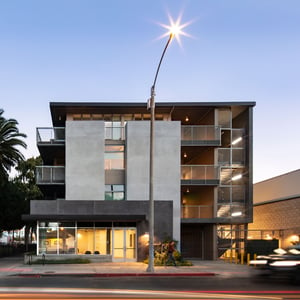 Dusk image of a well lit contemporary four story multi family building with a ground floor commercial space