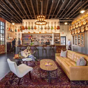 Retail guitar shop with colorful guitars hanging from the walls and a customer trying our a guitar on a stylish couch.