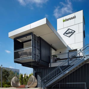 A Pavilion constructed of grey Shipping Containers and a central elevator tower with galvanized metal staircases.