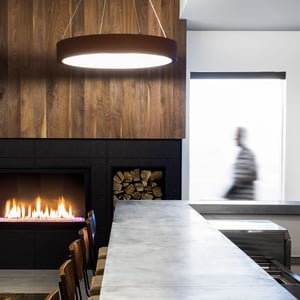 A polished concrete bar top with a circular hanging light fixture and fireplace with stacked fire wood
