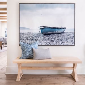 A bleached wood bench with pillows in front of a stylized photo of a boat in a hotel lobby
