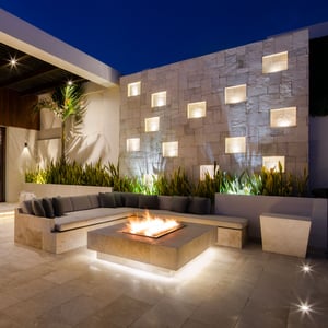 A romantic stone firepit with accent lighting appears to hover above the stone floor of an exquisite outdoor lounge space in Cabo San Lucas Mexico