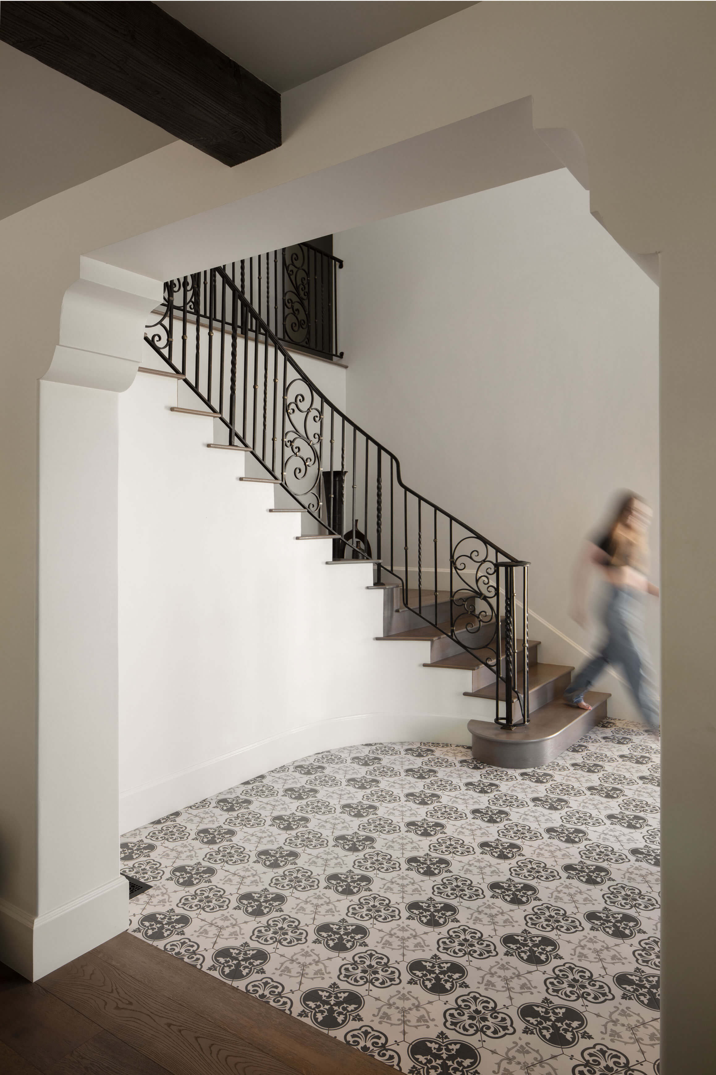 Traditional home design meets modern flow with decorative tile flooring and wrought iron stair rail in this Spanish Colonial Revival entryway.