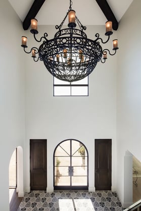 Dramatic arched doors and an ornate iron chandelier define the grand entry in this Spanish Colonial Revival inspired traditional home.