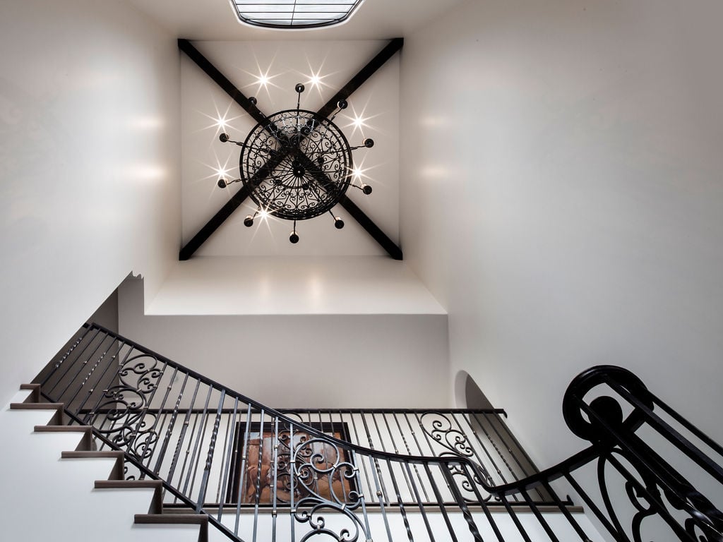 Wrought iron chandelier and exposed ceiling beams highlight Spanish Colonial Revival craftsmanship in a traditional home design staircase.