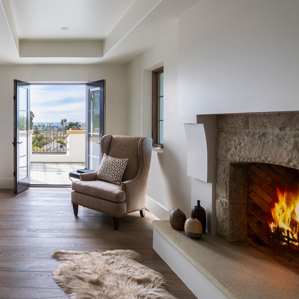 A cozy reading nook with fireplace opens to a terrace, merging traditional Spanish Colonial Revival elements with indoor-outdoor living.