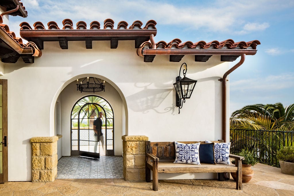 A classic arched entryway and wrought iron lantern exemplify traditional home design rooted in Spanish Colonial Revival style.