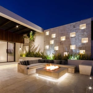 Glowing outdoor patio with firepit with stone wall backdrop with candle lit niches