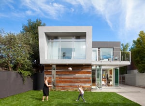 A woman and her daughter play with a ball in front of a modern two story home.