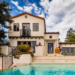 A classic Spanish Mediterranean style home sits above a sparkling blue green swimming poll adorned with terracotta tile and limestone