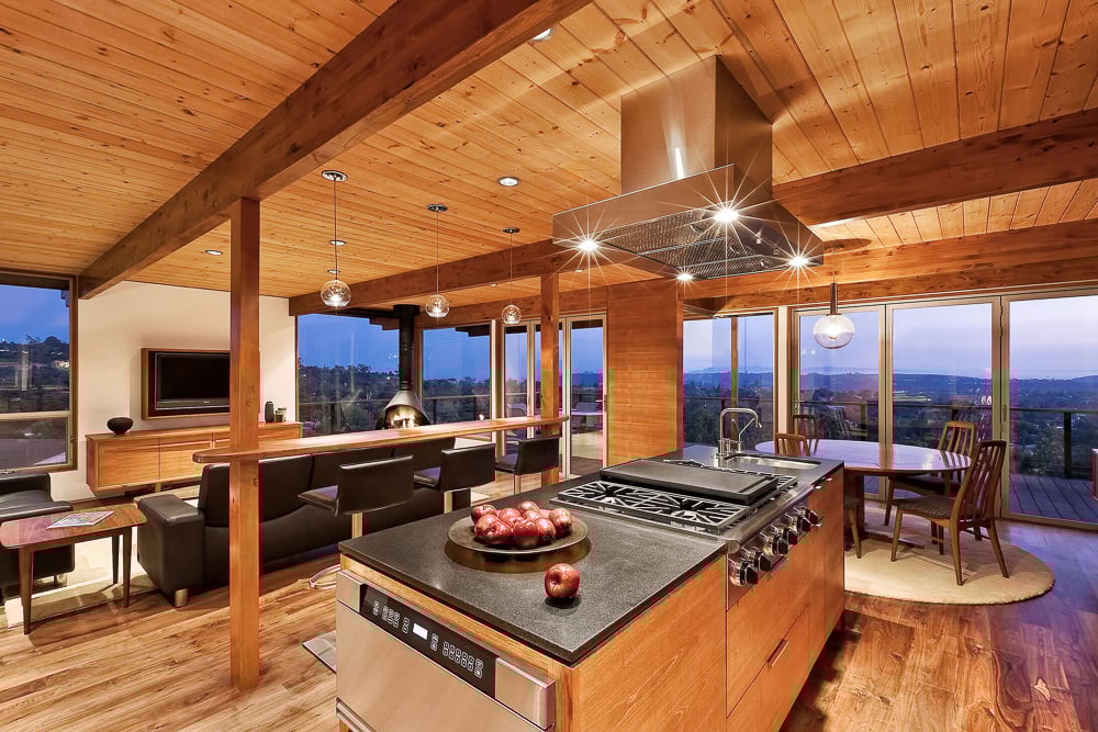 Open-concept kitchen and living room with wood-paneled ceilings and panoramic city views in a mid-century modern home.