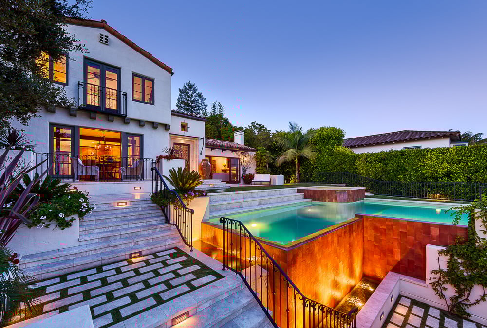 Multi-tiered Spanish-style home with illuminated pool and terraced steps, showcasing traditional home design and enduring architectural heritage.