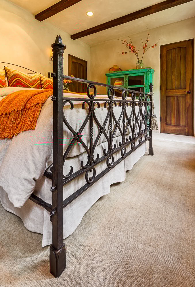 Custom iron bed anchors this traditionally styled bedroom, emphasizing craftsmanship tied to architectural heritage.