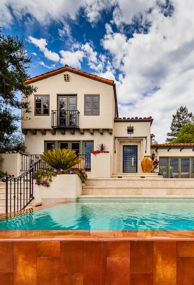 Two-story traditional home design featuring stucco façade, terracotta accents, and a formal pool entry rooted in architectural heritage.