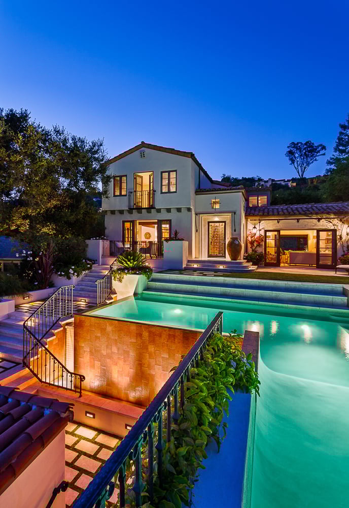 Evening view of traditional Santa Barbara-style residence with glowing pool, expressing architectural heritage through form and materiality.