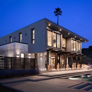 Modern residence built from four forty foot shipping containers stacked atop a concrete foundation face into the evening sunset with warm inviting interior spaced glowing in the dusk light