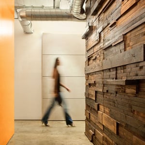 Picture of a modern wood industrial hallway with a woman walking and orange wall