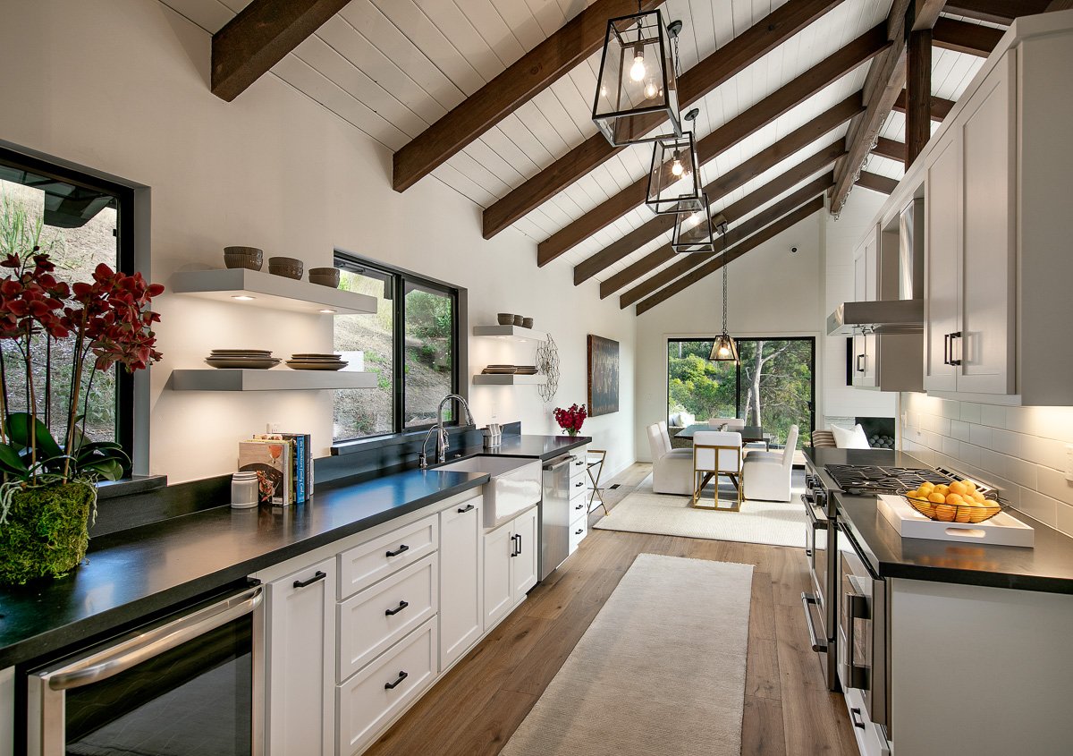 Sleek galley kitchen with dark countertops, open shelving, and vaulted ceiling—a prime example of residential remodeling within interior design.