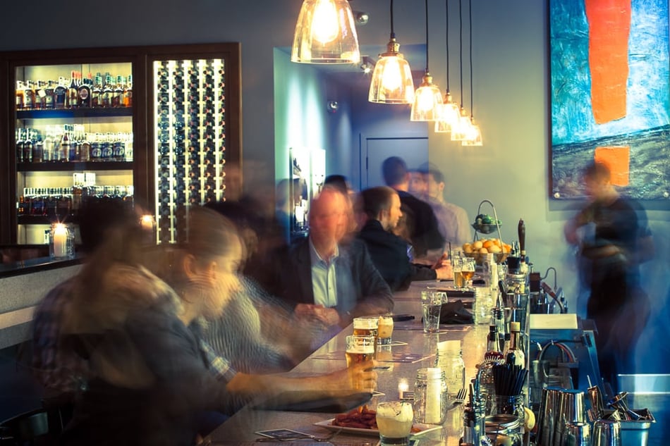 Bar area at Eureka! featuring curated backlit shelving, pendant lighting, and a bustling crowd.