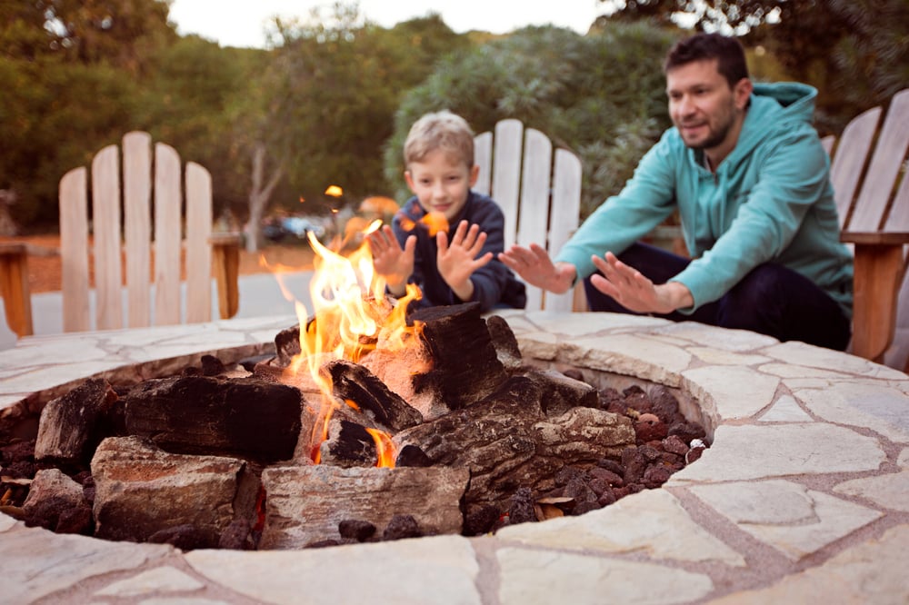 A father and son warm their hands at a fire pit, enjoying outdoor living elements that enhance a modern forever home design.