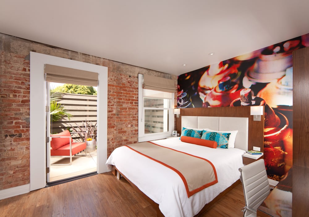 Boutique guest room at Hotel Indigo Santa Barbara featuring vibrant wall art, exposed brick, and access to private patio space.
