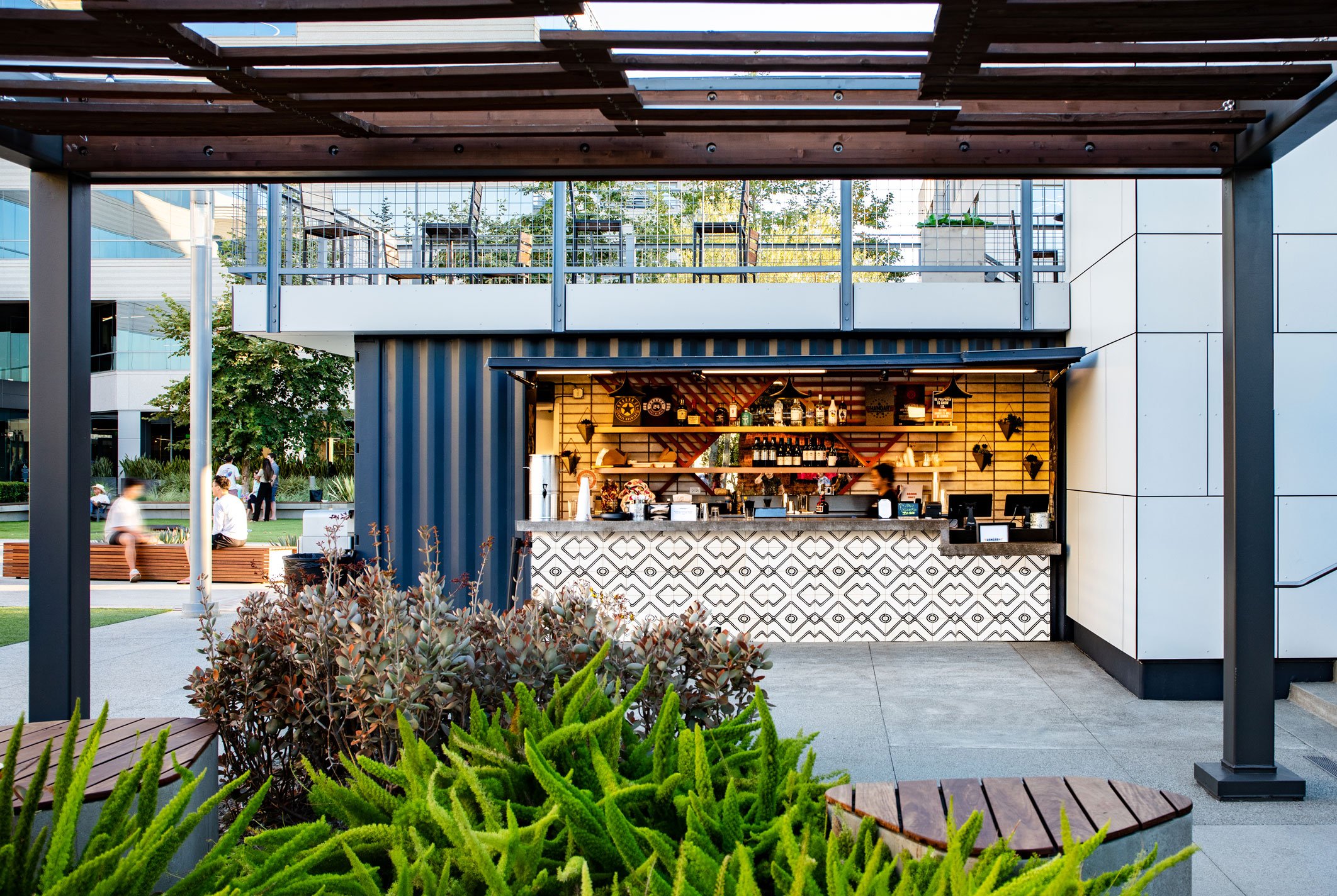 The Pavilion café transitions from daytime coffee to evening cocktails, featuring a hinged front façade that secures the modular structure after hours.