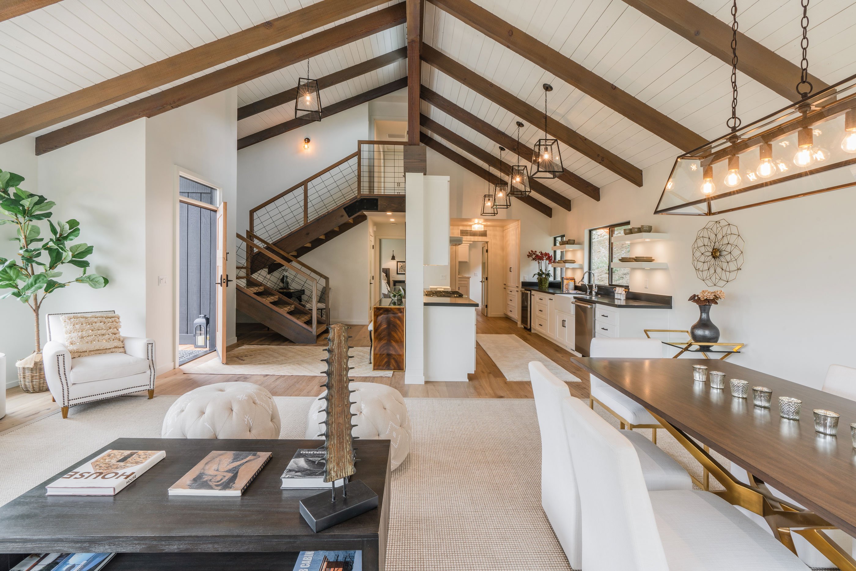 Open concept interior design in the main living area, featuring vaulted ceilings with exposed beams, modern lighting, and a seamless connection to the kitchen and dining spaces.