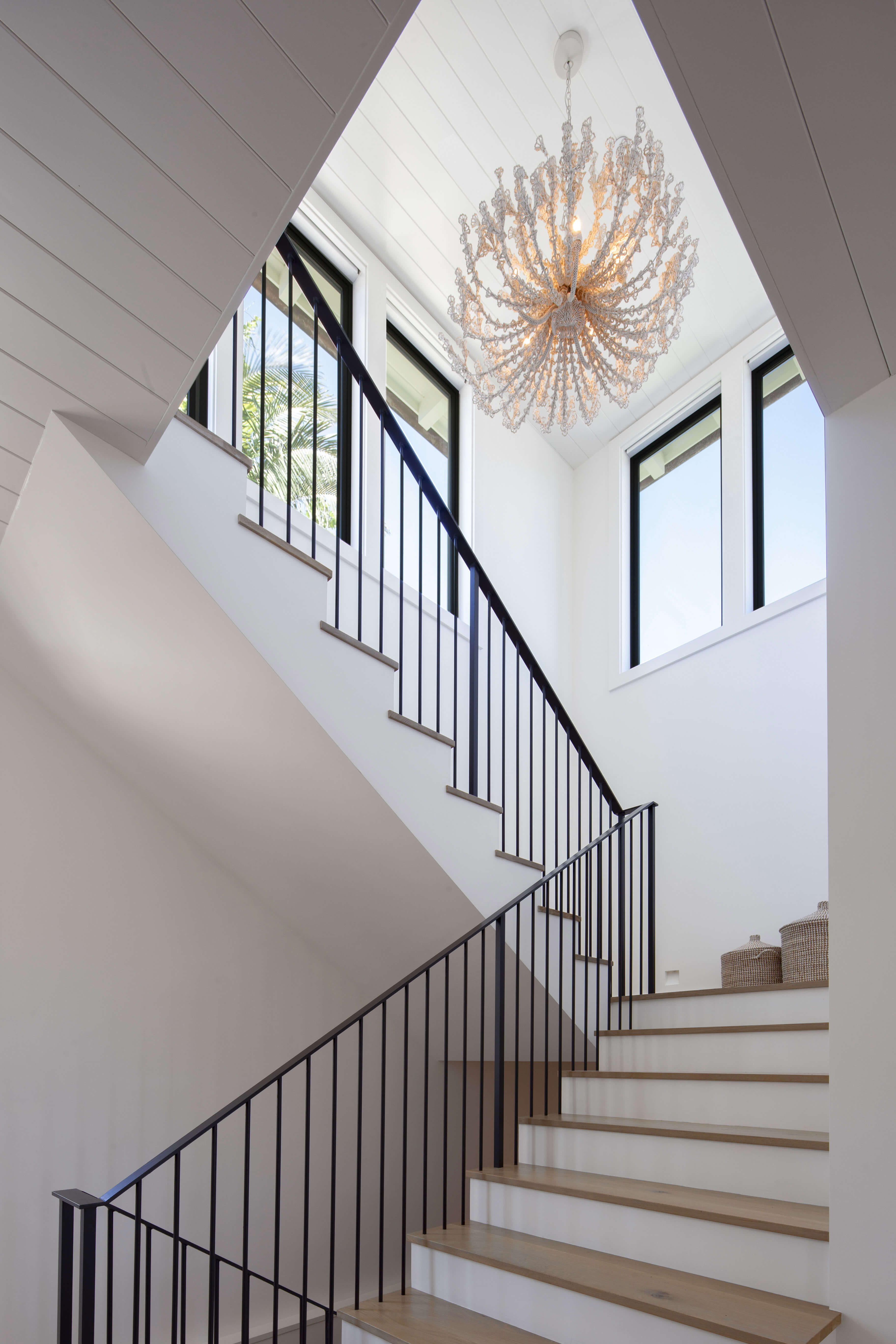 Light-filled stairwell featuring a sculptural chandelier and high windows in a traditional coastal residence.