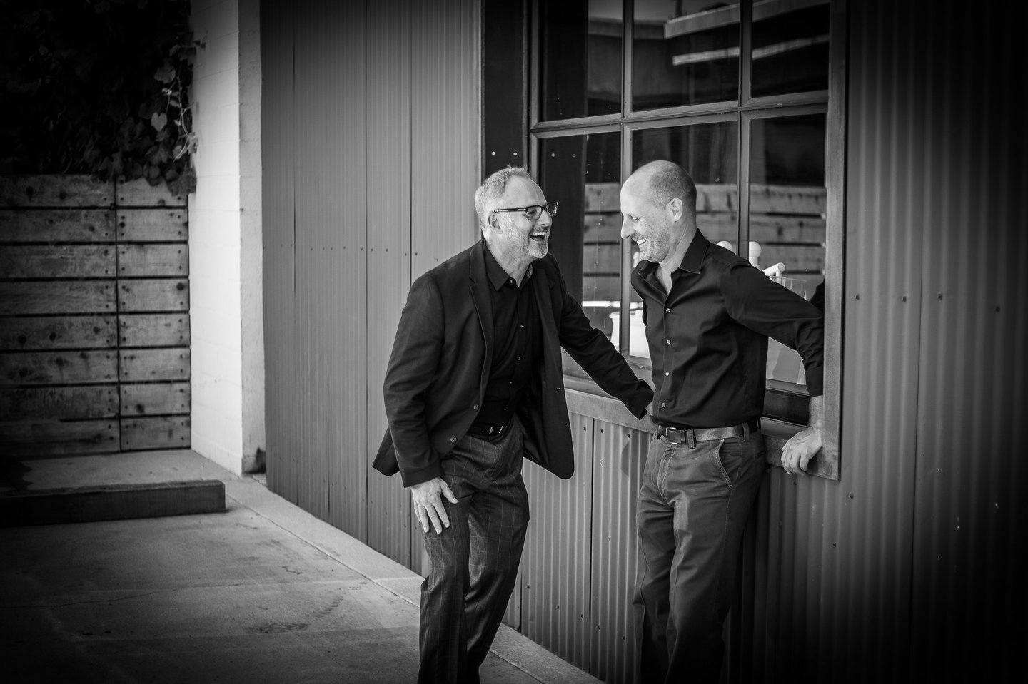 Architects Clay Aurell and Josh Blumer standing in the back of their studio laughing together.