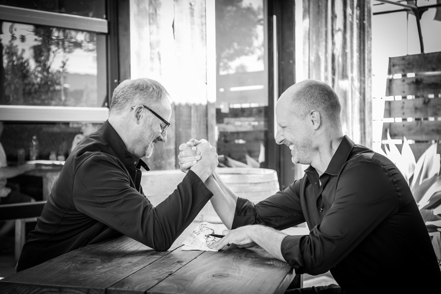 Architects Clay Aurell and Josh Blumer sit at a table playfully arm wrestling