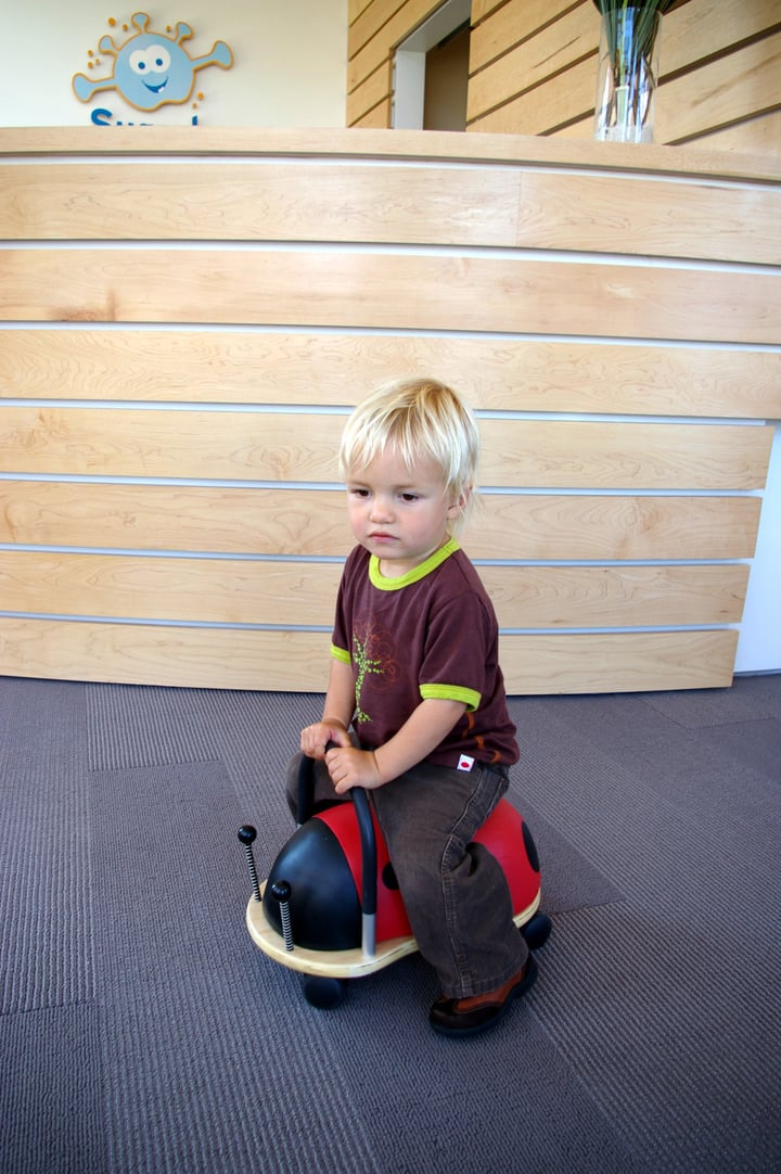 Sugarbug Dental-@2x-7b Toddler at reception desk on scooter