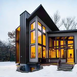 A modern forest home nestled in the snow with tall windows and golden light