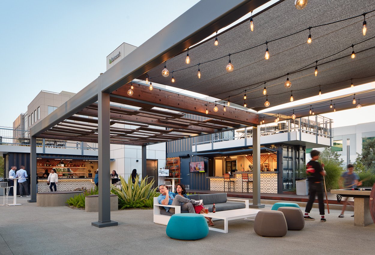 Outdoor gathering space under custom trellises complements the modular café experience.