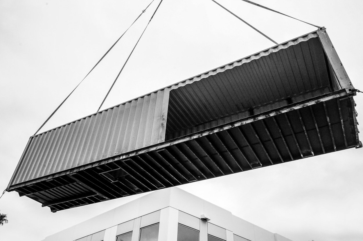 Shipping containers are craned into place during the on-site installation of the Pavilion.