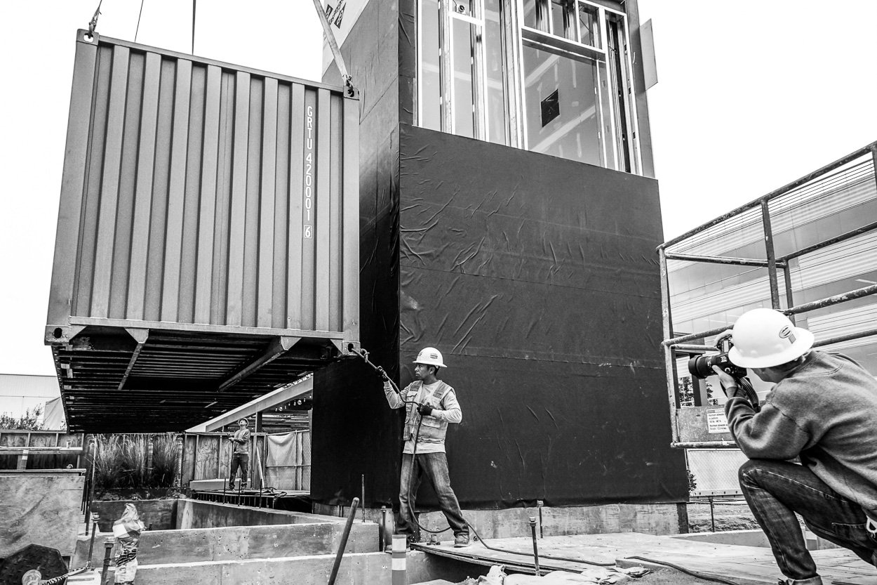 Shipping containers are craned into place during the on-site installation of the Pavilion.