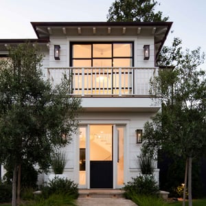 A brick pathway leads to an inviting Dutch entry door on a beachside craftsman style home with white lap siding, standing seam metal roof and slim steel framed windows